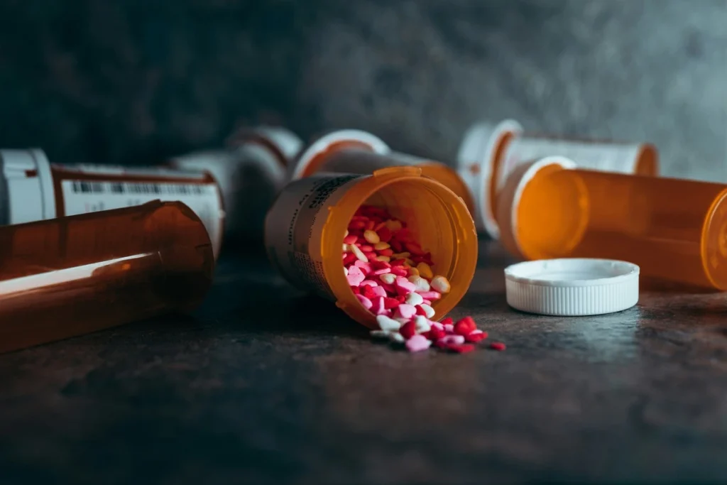 Wellcare Online Drug Rehab 4 Spilled prescription bottles with colorful pills on a dark surface, representing substance use and the need for professional online drug rehab support.