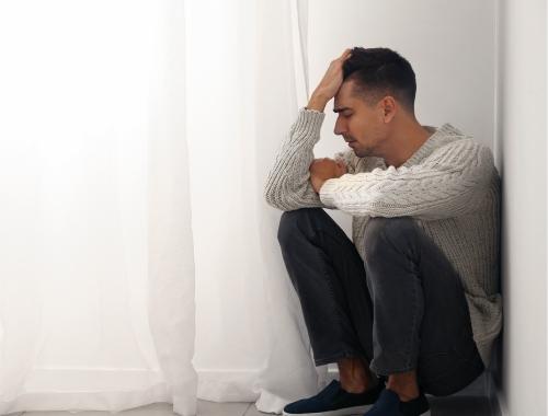 A man with an addiction is crouching in a corner at home during a mental health crisis