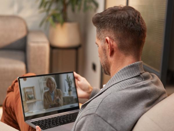 A mam sits a home with a laptop to attend a remote therapy session