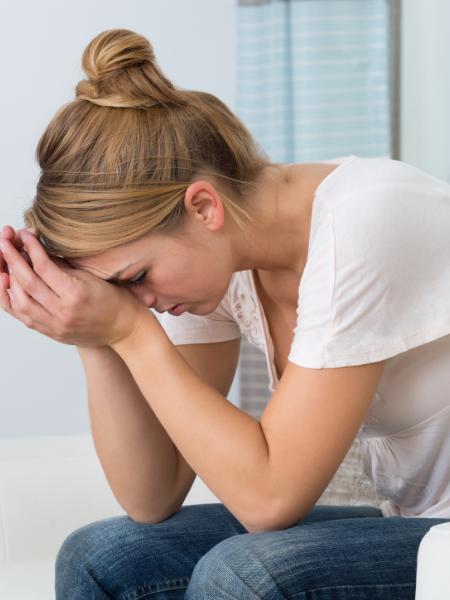 A woman sits with her hands partially covering her face, due to anxiety from prescription drug addiction
