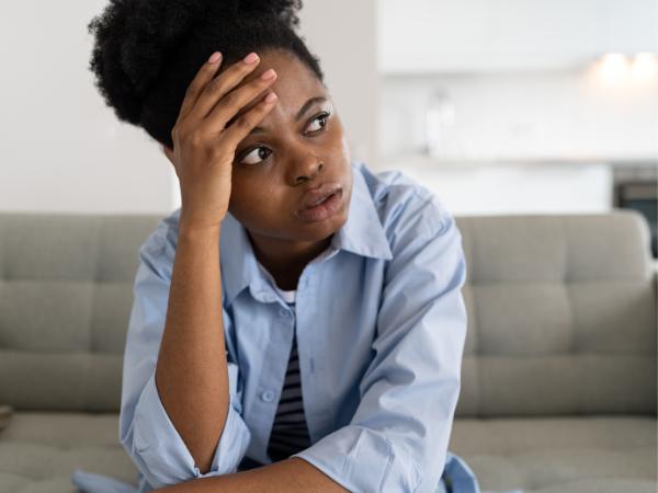 An anxious woman sitting on a couch with one hand on her forehead