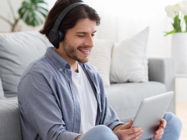 A man holding a tablet while sitting on the floor against the couch during a drug rehab video call