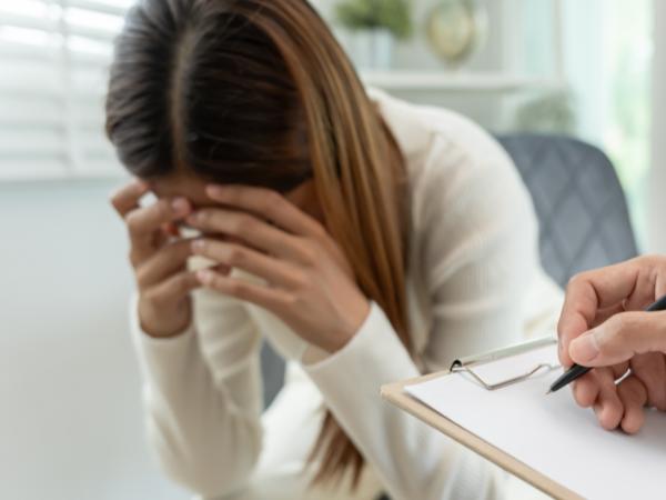 A woman sitting with her head down and hands over her face during a mental health assessment