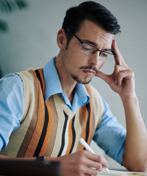A man sits at a table and takes notes about his mental health needs for online vs. in-person therapy