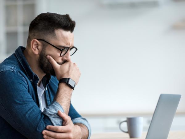 An anxious man looking at his laptop and listening to his therapist during a mental health videoconference