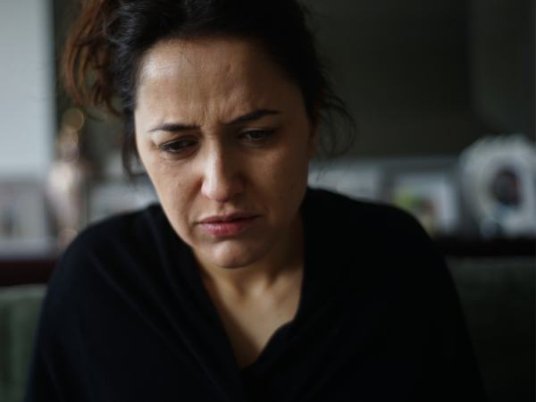 A middle-aged woman sitting at home, frowning due to illness from prescription synthetic drug addiction