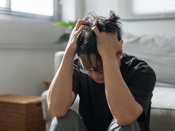 A man with a substance addiction is sitting on the floor with his face down, holding his head