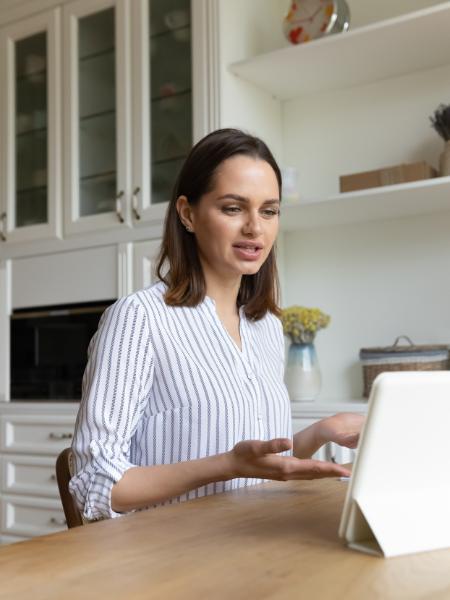 A woman sits at a kitchen table and talks to her therapist during an online session