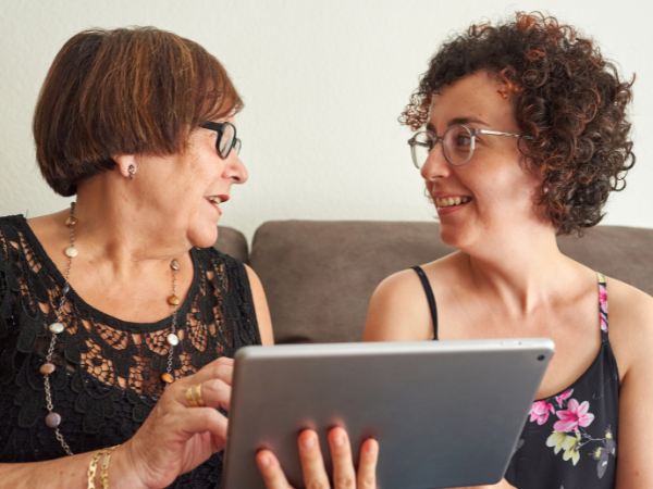 A senior mom and adult daughter share a table for virtual mental health therapy