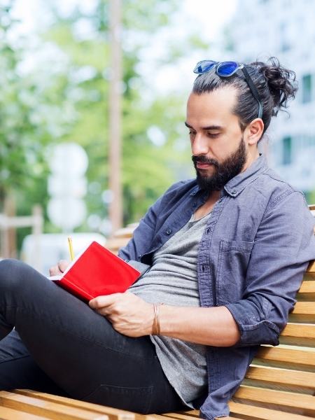 A man sitting outdoors on a bench making notes about mental health and addiction therapy options