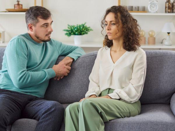 A man sitting on a couch, looking at a woman as they have a conversation about rehab