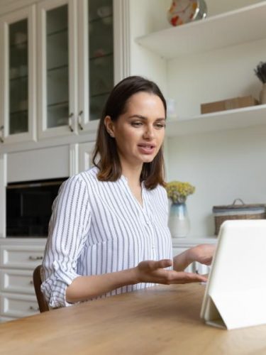 A woman sits at a kitchen table and talks to her therapist during an online session
